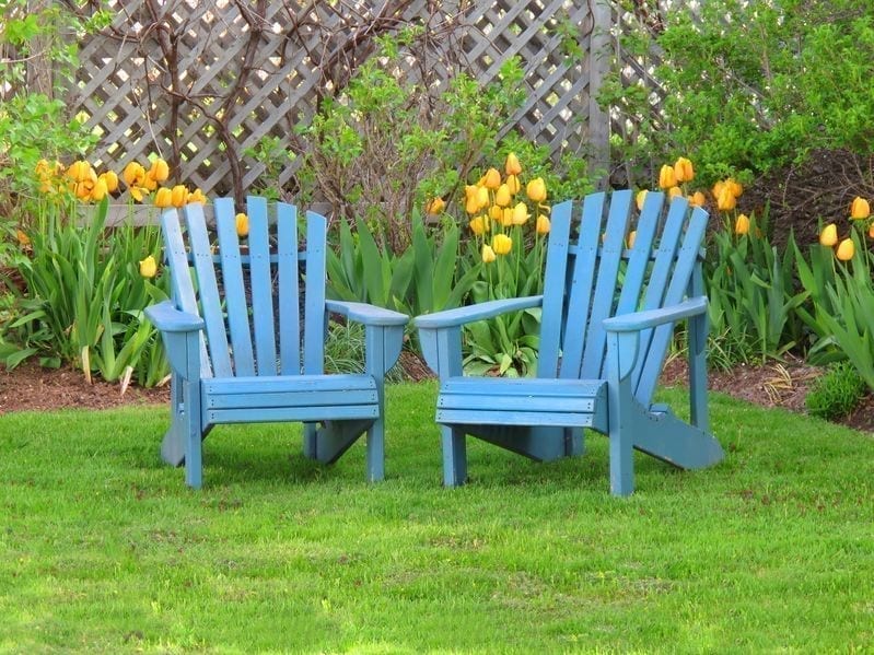 two wooden lawn chairs in a nice yard with flowers